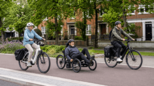 Two people on ebikes, and one man on a mobility electric tricycle between them on a quiet british road